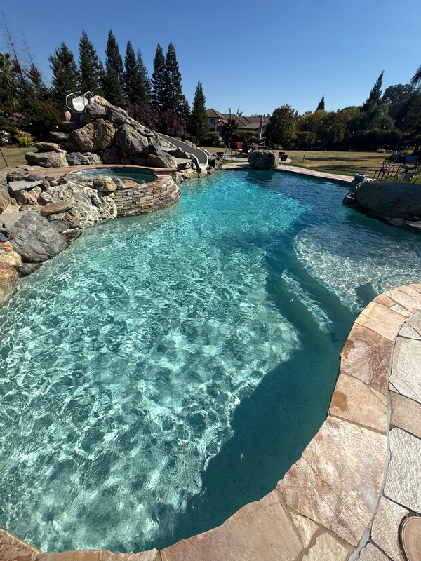 Backyard pool with a rock grotto, water slide, raised spa, and flagstone coping